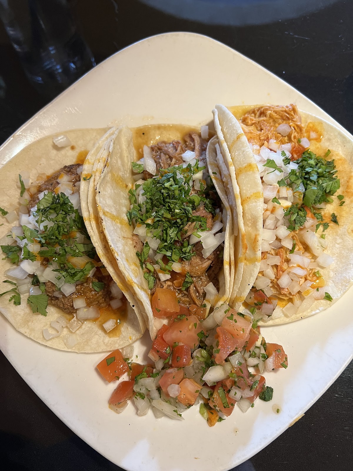A plate of street tacos topped with cilantro and onion